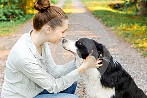 Smiling young attractive woman playing with cute puppy dog border collie on summer outdoor background. Girl holding