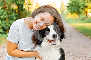 Smiling young attractive woman playing with cute puppy dog border collie on summer outdoor background. Girl holding