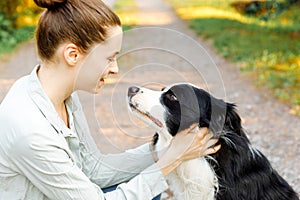 Smiling young attractive woman playing with cute puppy dog border collie on summer outdoor background. Girl holding embracing