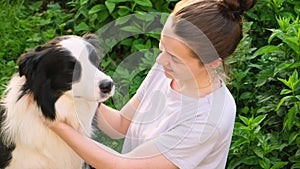 Smiling young attractive woman stroking playing with cute puppy dog border collie on summer outdoor background. Owner