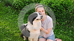 Smiling young attractive woman stroking playing with cute puppy dog border collie on summer outdoor background. Owner