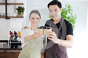 Smiling young barista couple loves Asian man and caucasian woman holding cups of hot coffee together. Start up Coffee shop and