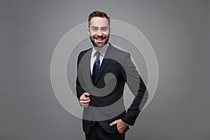 Smiling young bearded business man in classic black suit shirt tie posing isolated on grey background studio portrait