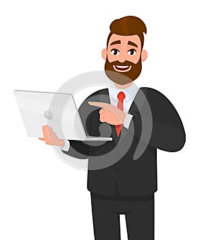 Smiling young bearded business man holding/showing latest brand new laptop computer device and pointing it with hand finger.