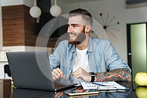 Smiling young bearded man working on laptop computer