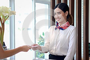 Smiling young beautiful Asian female receptionist giving key card to customer hand at hotel reception counter desk, check in hotel