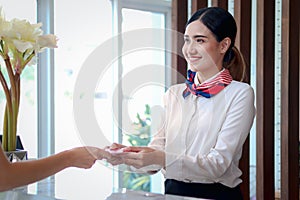 Smiling young beautiful Asian female receptionist giving key card to customer hand at hotel reception counter desk, check in hotel