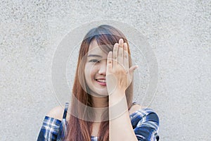 Smiling young beautiful asian woman closing her eyes with hands on concrete wall background.