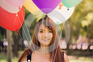 Smiling young beautiful asian women with long brown hair in the park. With rainbow-colored air balloons