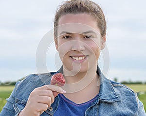 Smiling young beautiful woman with red tasty strawberry on the field