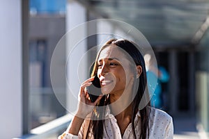 Smiling young biracial businesswoman talking on mobile phone in corridor at workplace