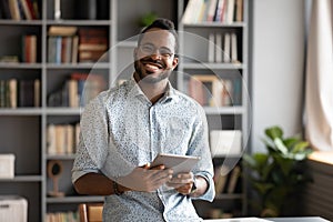 Smiling young biracial man in glasses holding digital computer tablet.