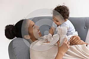 Smiling young biracial mom relax on couch with little baby