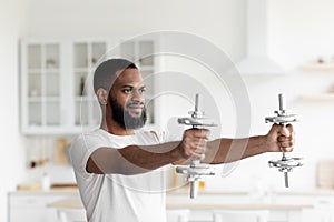 Smiling young black bearded athlete man in white sportswear doing hands exercise with dumbbells