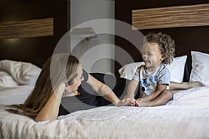 A smiling young black boy and his mother playing together on a bed indoors