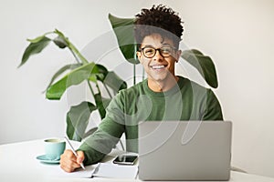 Smiling young black guy using laptop computer at cozy cafe