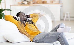 Smiling Young Black Guy Wearing Headphones Relaxing On Couch In Living Room