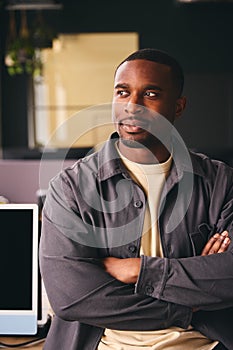 Smiling Young Black Male Standing In Office Looking Away From Camera With Arms Crossed