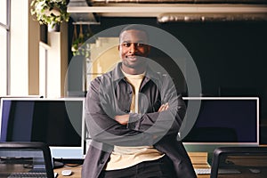 Smiling Young Black Male Standing In Office Looking At Camera With Arms Crossed