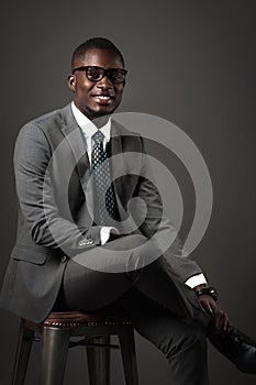 Smiling young black man sits with glasses and gray business suit