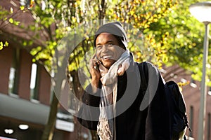 Smiling young black man walking in city with mobile phone and bag during autumn