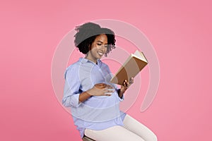 Smiling young black pregnant woman in casual with big belly reading book