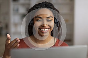 Smiling young black woman with headset communicating by video call on laptop photo