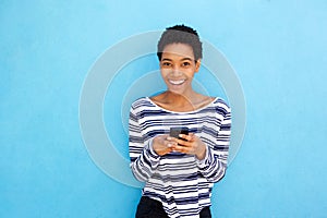 Smiling young black woman holding cellphone by blue background