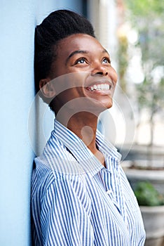 Smiling young black woman leaning against wall and looking up