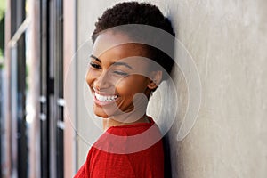 Smiling young black woman leaning against wall outside