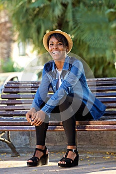 Smiling young black woman sitting on bench at the park