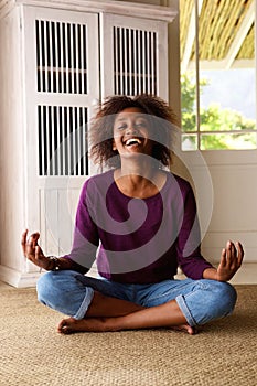 Smiling young black woman sitting on floor practising yoga