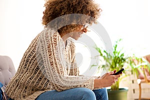 Smiling young black woman sitting on sofa looking at mobile phone