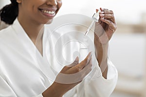 Smiling Black Woman Using Moisturizing Serum While Making Beauty Treatments At Home