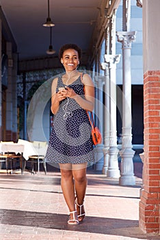 Smiling young black woman walking with cellphone and earphones