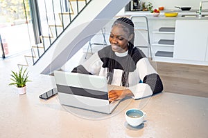 Smiling Young Black Woman Working on Laptop in Stylish Kitchen