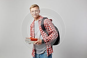 Smiling young blond guy with black backpack on his shoulder dressed in a white t-shirt, red checkered shirt and jeans