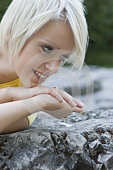 Smiling young blond woman lying on a rock