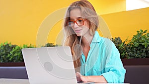 Smiling young blond woman working on laptop in cafe