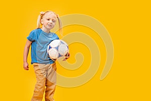 Smiling young blonde girl holding soccer ball against yellow background. Child and football. Copy space, mockup