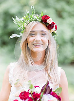 Smiling young blonde in red wreathe stands in the forest