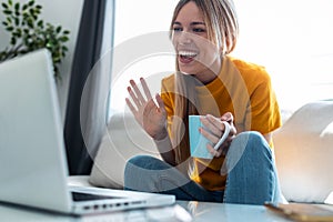 Smiling young blonde woman having videocall on laptop sitting on the couch photo