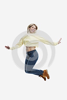 Smiling young blonde woman in jeans and a yellow sweater is jumping. Activity and positivity. Isolated on white background.