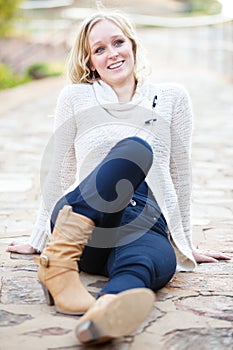 Smiling young blonde woman relaxing on pavement