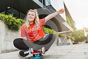 Smiling young blonde woman sitting on her skateboard, sun-flare in the corner of the photo