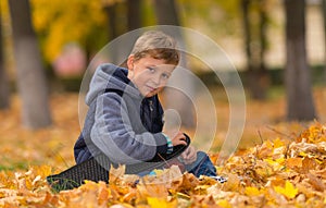 Smiling young boy sitting in park with skateboard.
