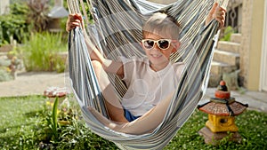 A smiling young boy relaxes in the hammock's gentle sway in a garden, encapsulating the feelings of summertime