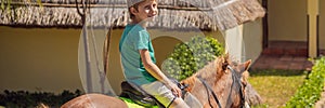 Smiling, young boy ride a pony horse. Horseback riding in a tropical garden BANNER, LONG FORMAT