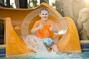 Smiling Young boy riding down a water slide showing a thumbs up