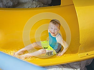 Smiling Young boy riding down a yellow water slide